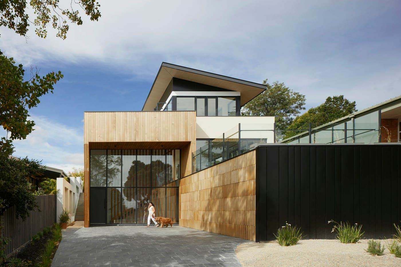 Timber and glass house with a black-clad wing and sandy garden
